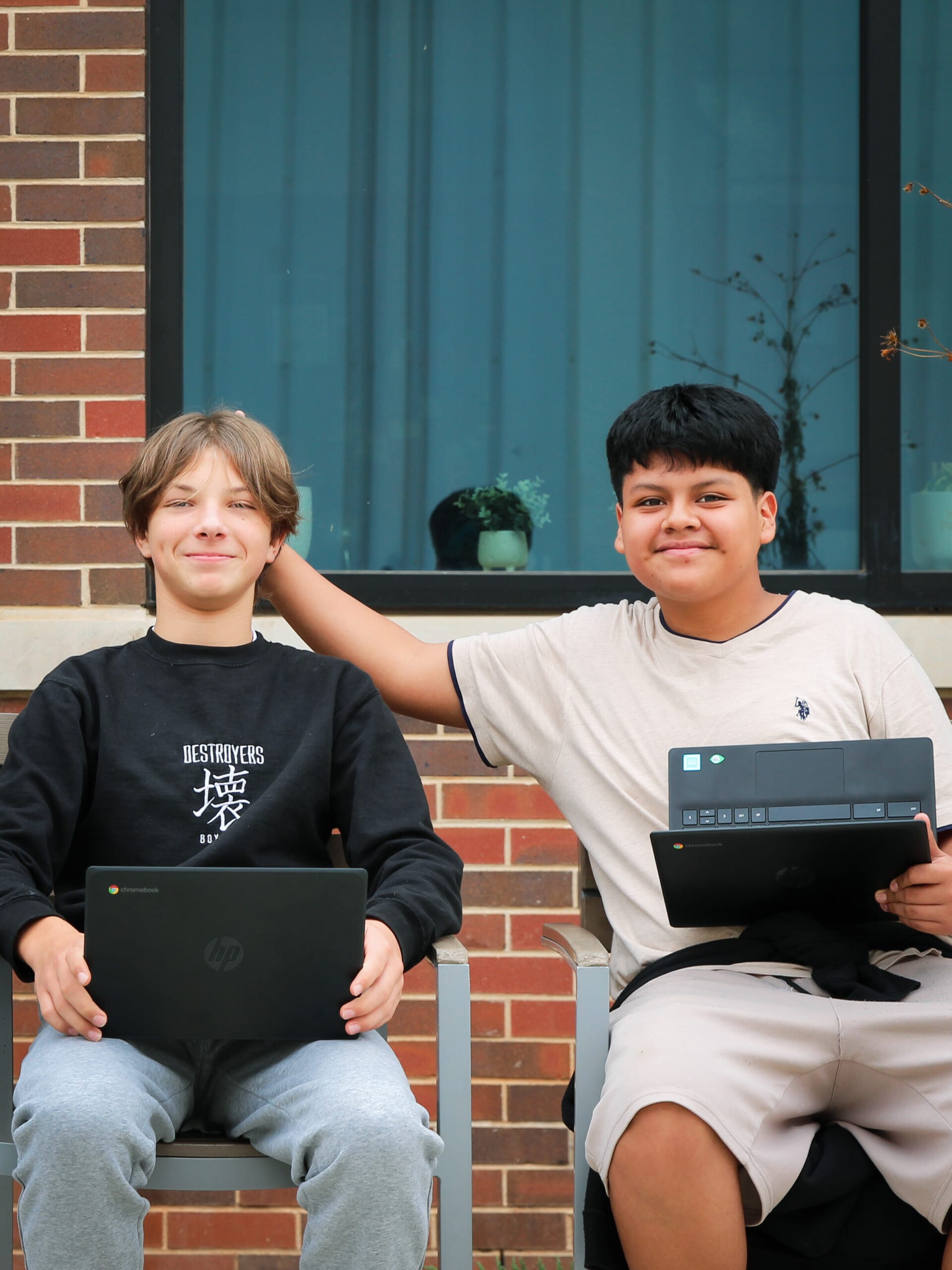 Two smiling students sitting outdoors holding Chromebook laptops