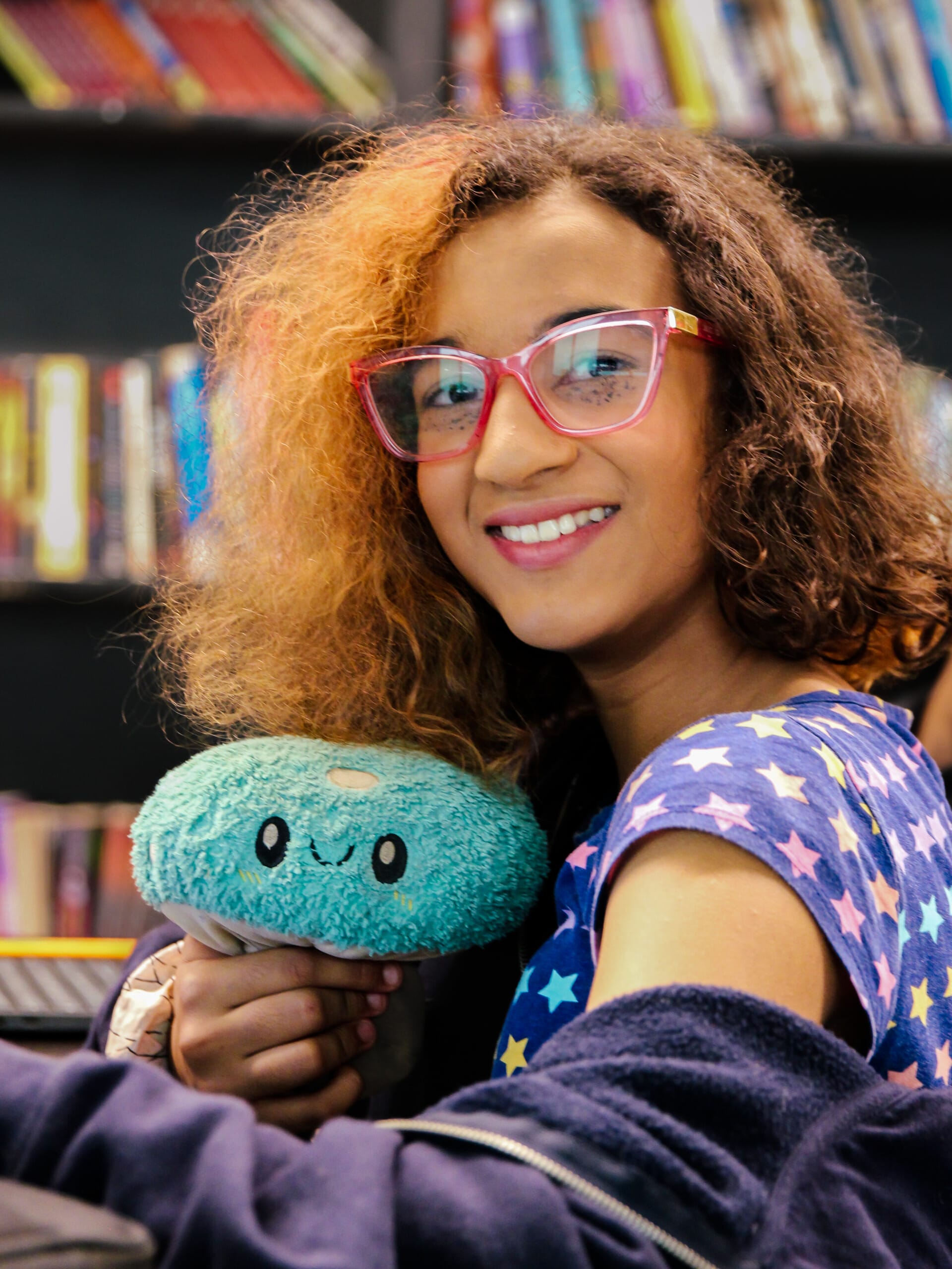 Smiling girl with glasses holding a teal mushroom plush toy