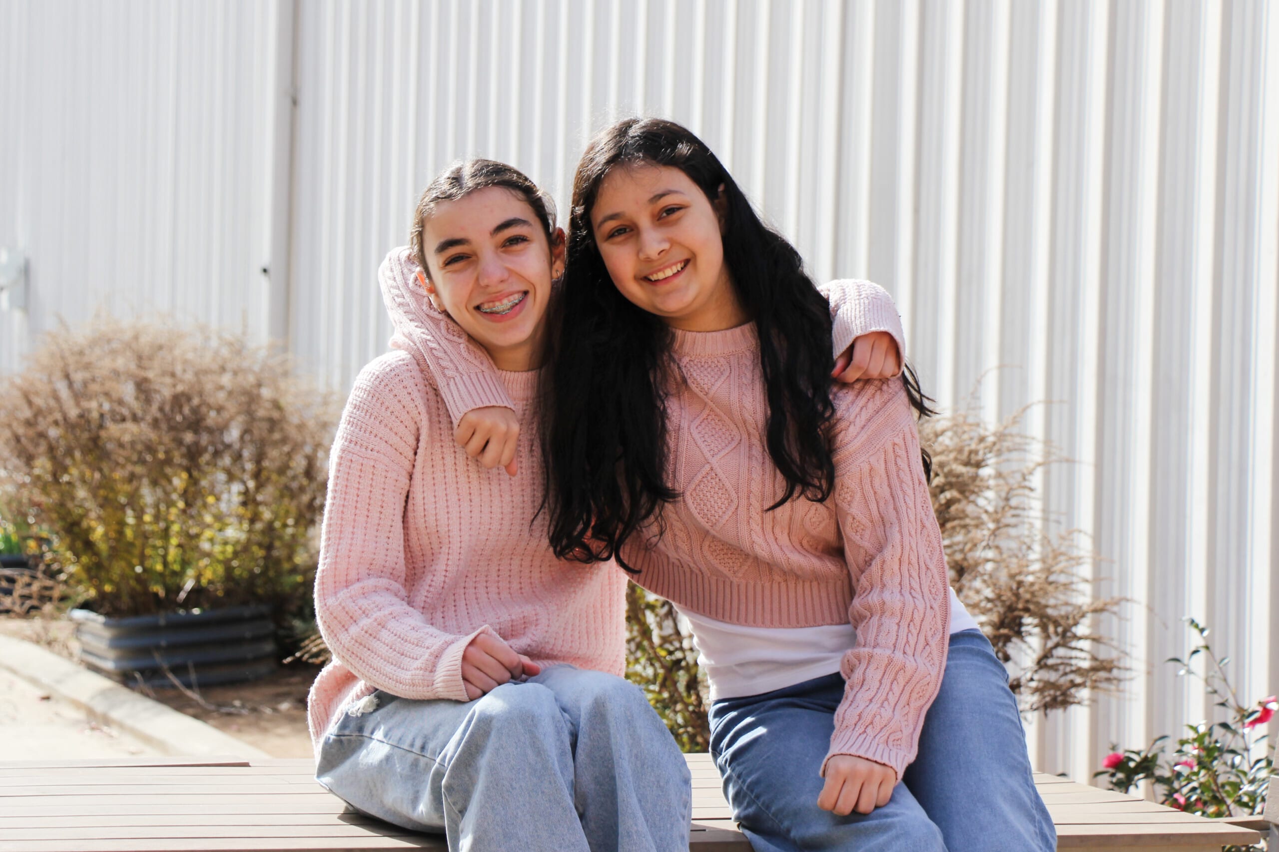 Two smiling teenage girls in matching pink sweaters sitting together
