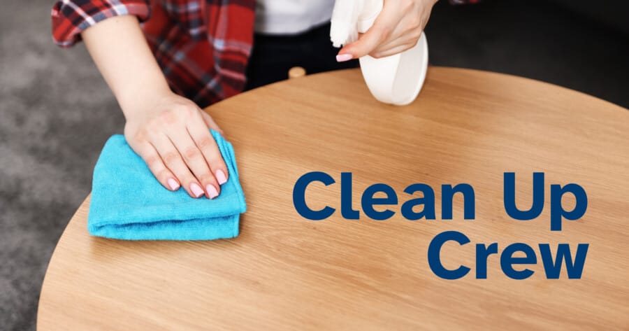 Clean Up Crew person wiping wooden table with blue cloth