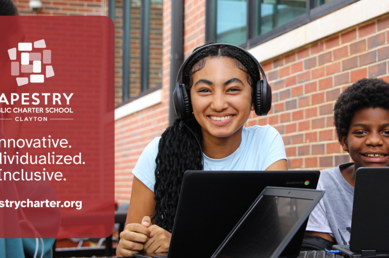 Students using laptops outdoors at Tapestry Public Charter School Clayton, smiling and engaged in learning in front of a brick school building.